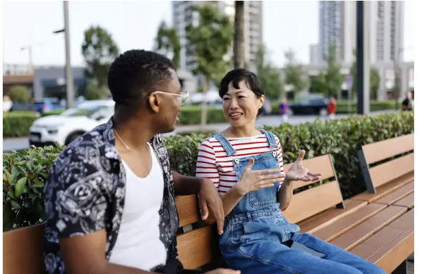 Two people sit on a park bench talking and gesturing.